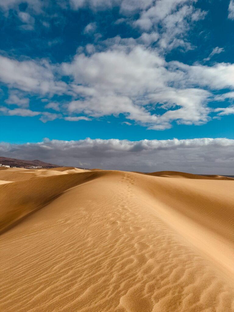 Stunning view of golden sand dunes under a bright blue sky in Maspalomas, Canary Islands.